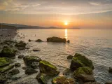 Golden hour sunset at Colwyn bay, North Wales. Warm sky and gentle waves along a rocky coastline.