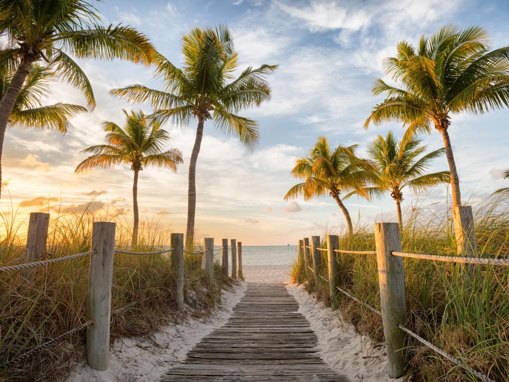 Sunrise at  Smathers Beach in Key West, wooden footbridge leading to the sand with palm trees either side