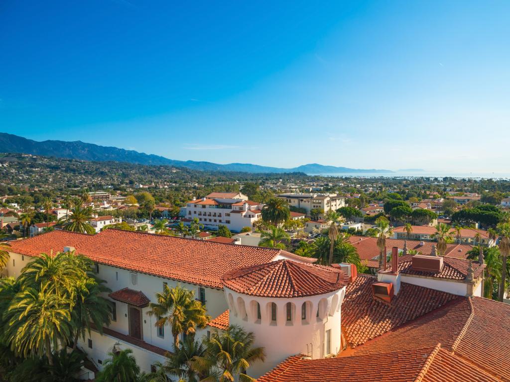 Santa Barbara, California, USA with a view of the Court House Buildings, Orange Roofs and Pacific Ocean in the distance against a blue sky.