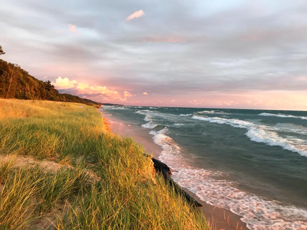 Lake Michigan, USA with a beach and a sandy path winding along the shore of Lake Michigan with a sunset horizon and sand dunes as a backdrop. 