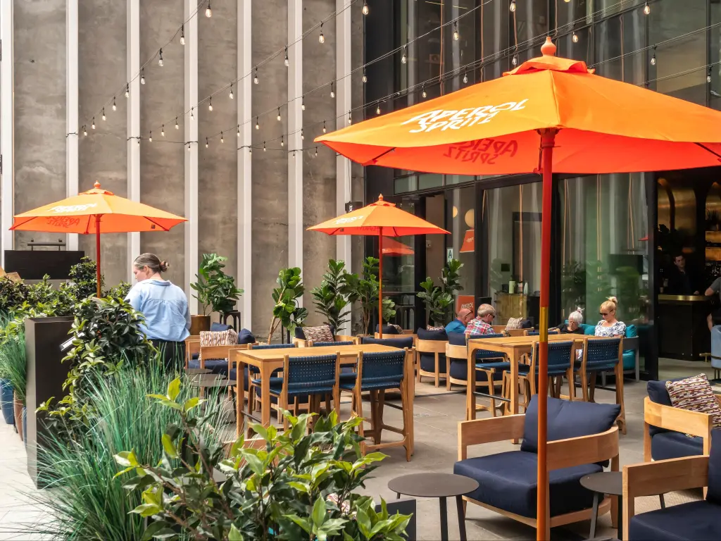 The al fresco dining area of a Motto by Hilton hotel in Chelsea in New York dotted with bright orange Aperol Spritz umbrellas