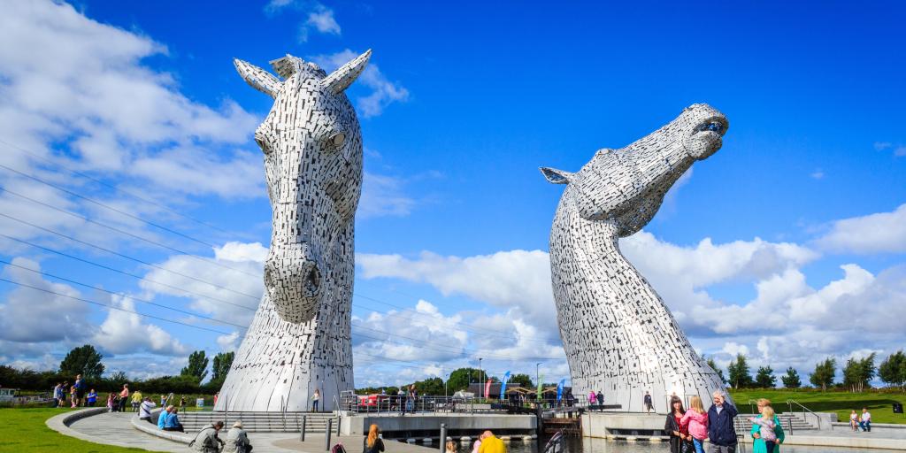 The giant horse heads of the Kelpies statue by Andy Scot tower over visitors to Helix Park on a sunny day in Falkirk, Scotland