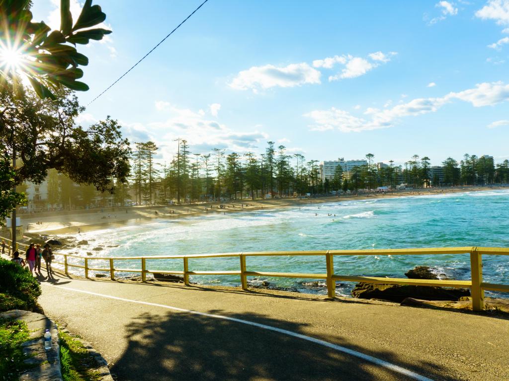 Coastal walkway in bright sunshine - blue sea with surf illuminated in the background