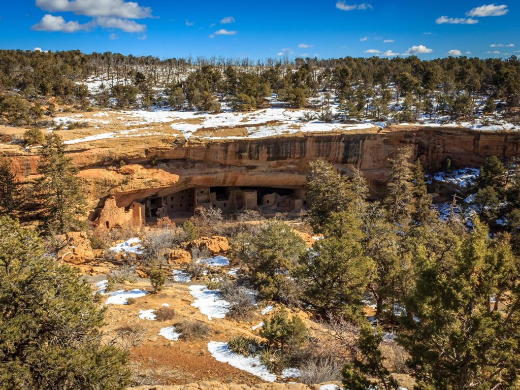 Spruce Tree House in Mesa Verde National Park, Colorado, in winter, with a dusting of snow covering the yellow-orange rocks and vegetation