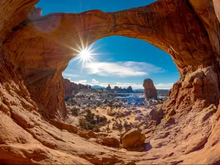 Double Arch in Moab, Utah, USA with snow and a sun star in a blue sky.