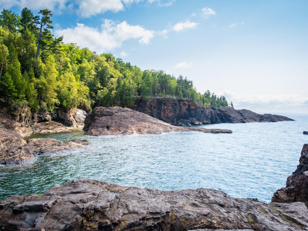Lake Superior, with green trees and gray cliffs of Presque Isle Park.