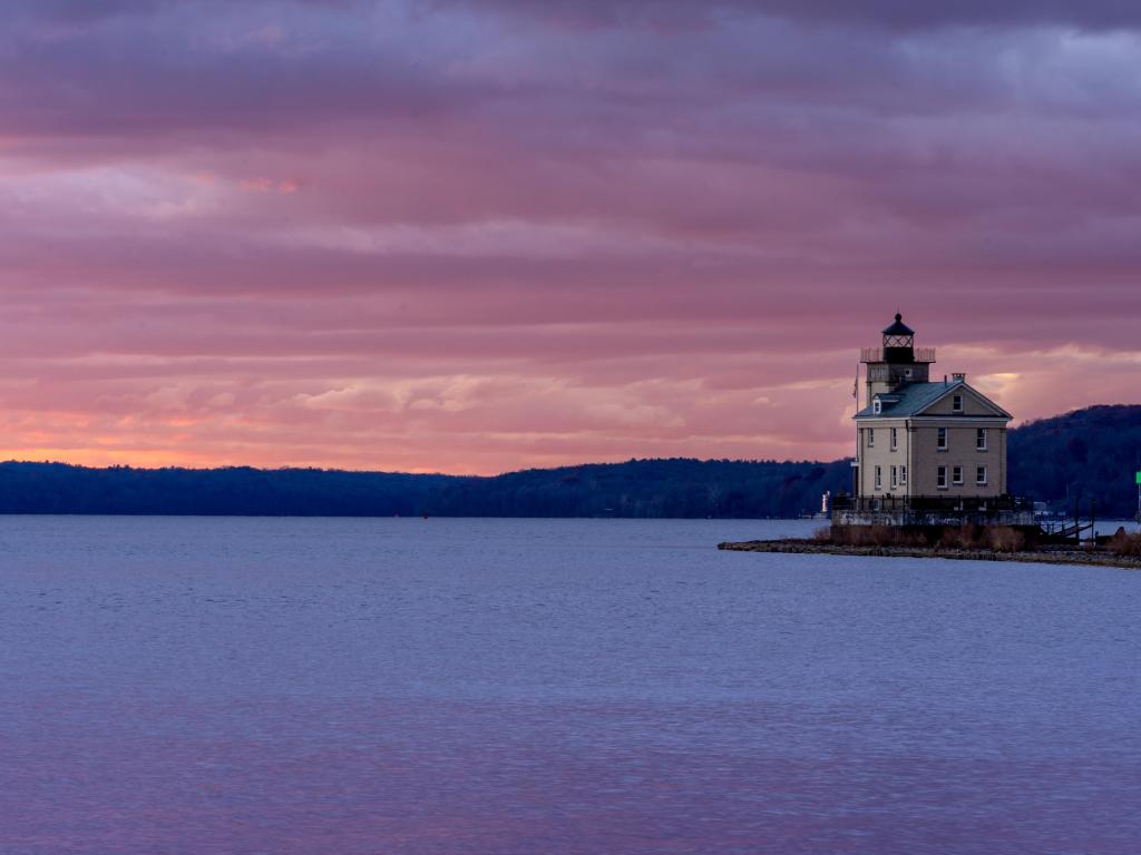 Square lighthouse on the bank of wide river with pink sunset