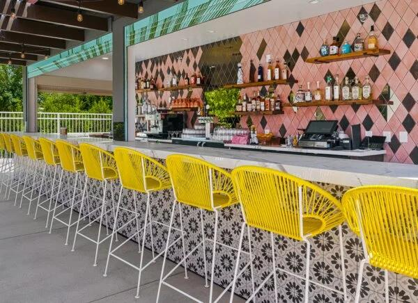 Vibrant outdoor bar area at The Paloma Resort, with bright yellow bar stools and fully stocked bar