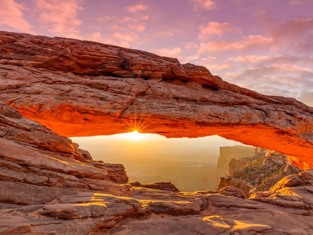 Sunrise sending a vibrant ray of light through arch-shaped orange-colored rock formation