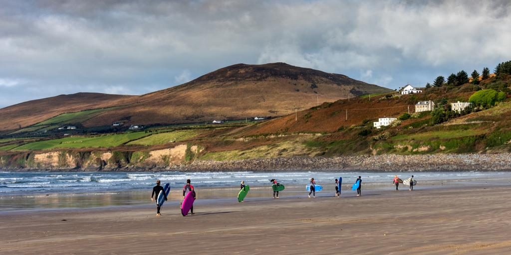 Surfers walking down Inch Beach in Ireland carrying their boards