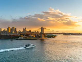 A ferry crossing the river towards Brooklyn Bridge at sunset