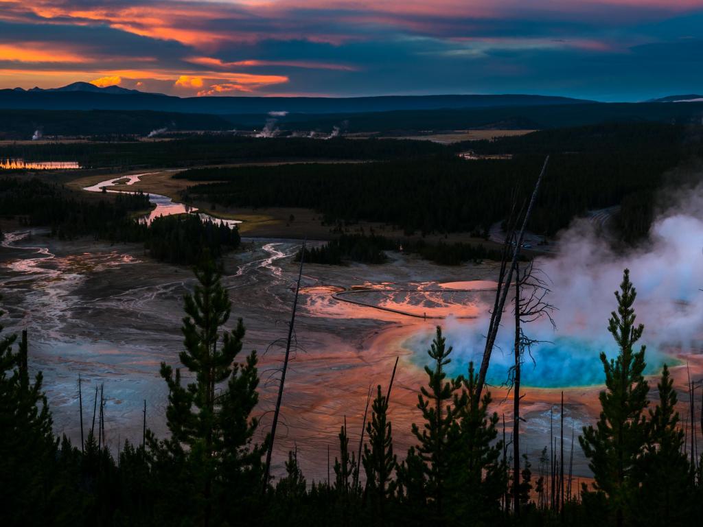 Yellowstone National Park, USA taken after sunset at the Grand Prizmatic Overlook with trees in the foreground and the steam from the craters in the distance. 
