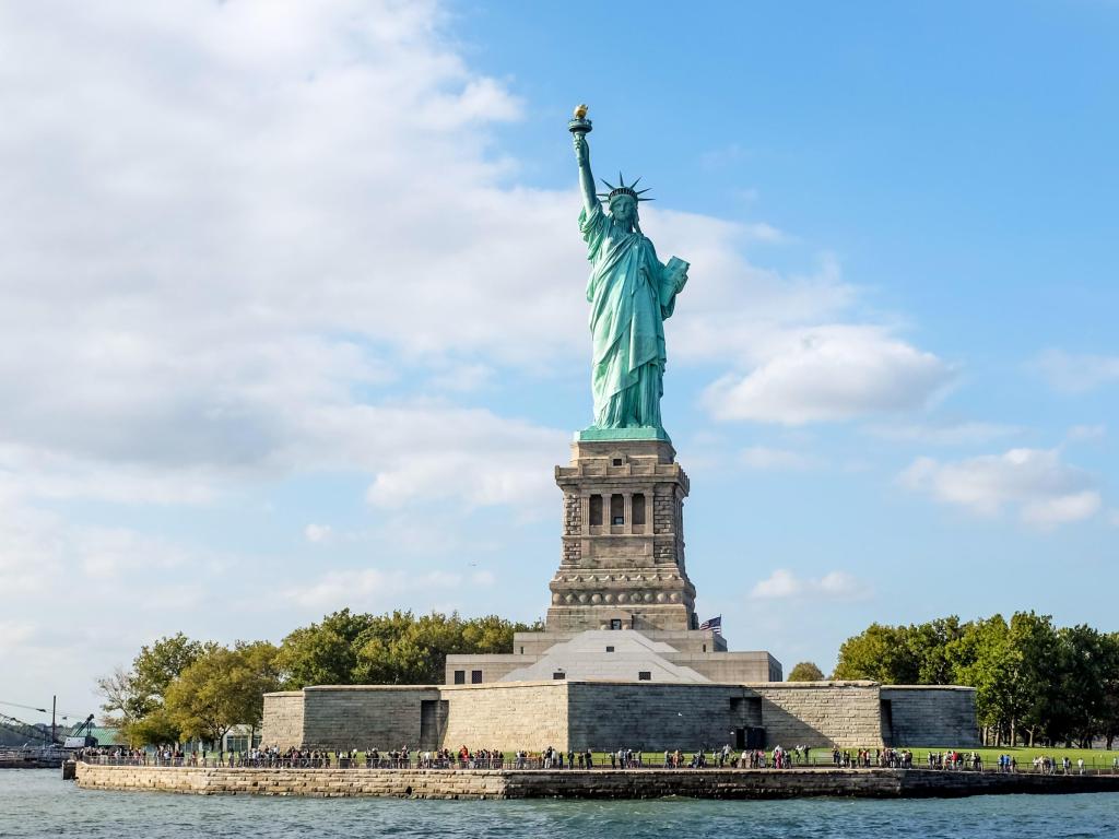 Front view of The Statue of Liberty with visitors standing along edge of Liberty Island, New York