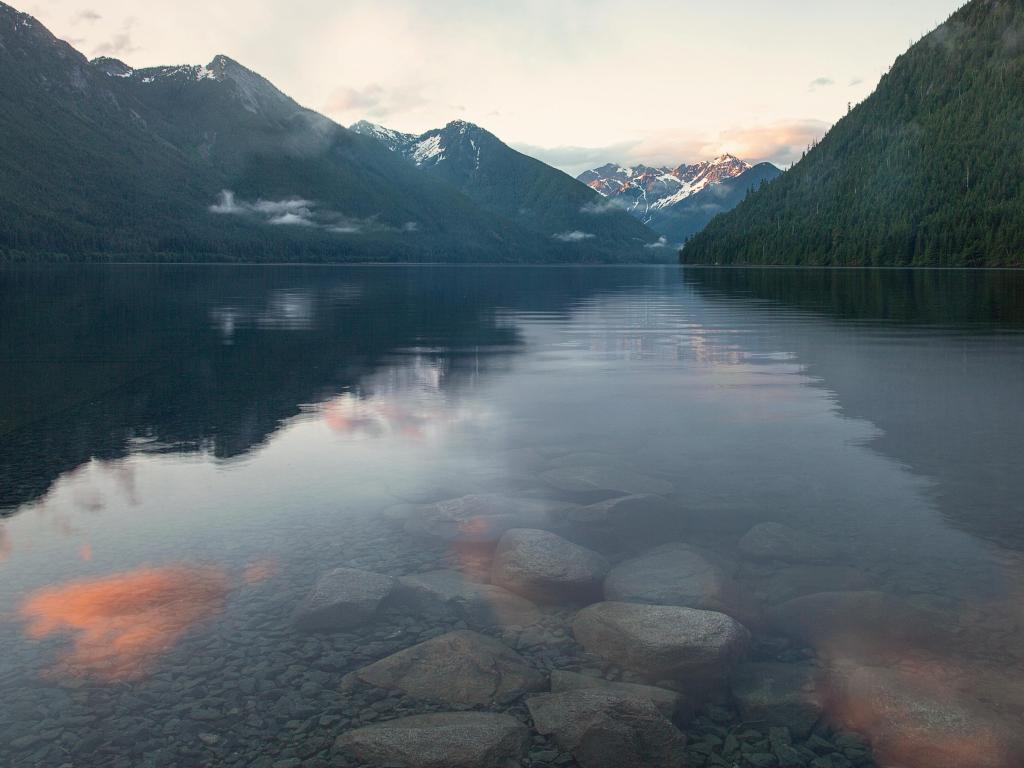 Chilliwack Lake, BC Canada taken during a warm sunrise over the calm lake with mountains in the distance reflecting in the water.