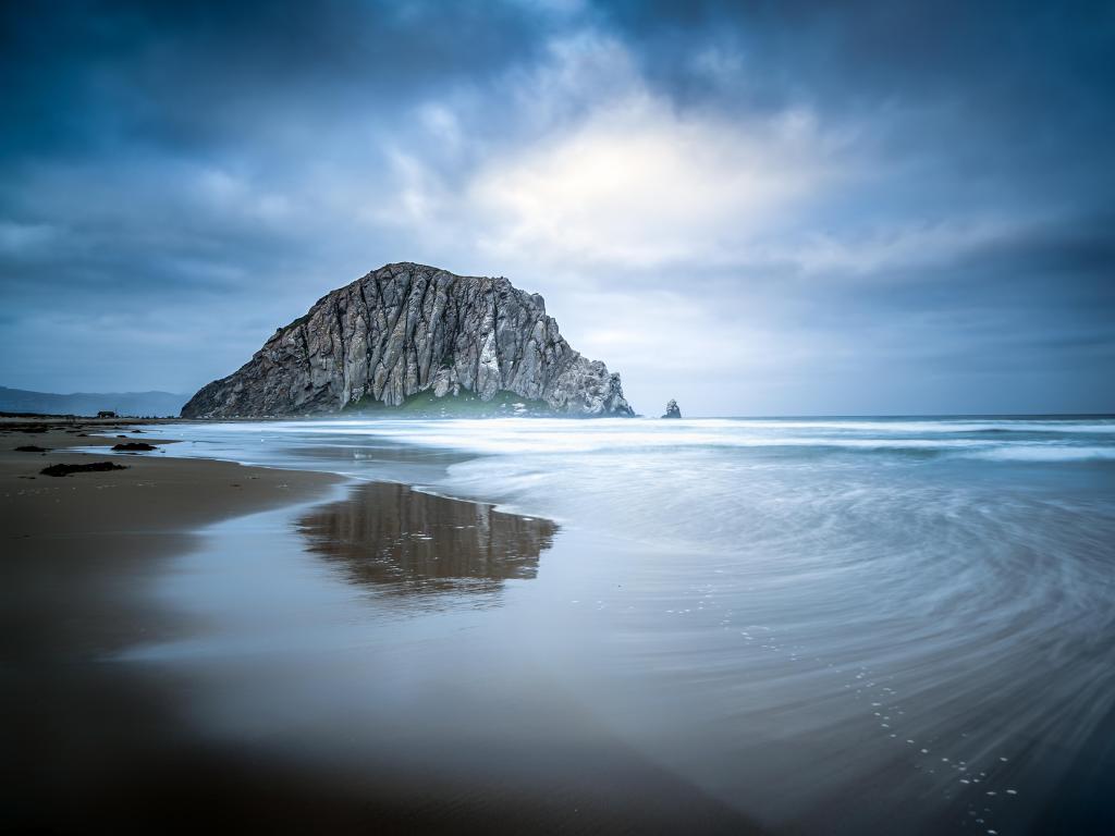 Stormy sky over the famous rock of Morro Bay in California. Shot during low tide with the rock reflecting on the beach.