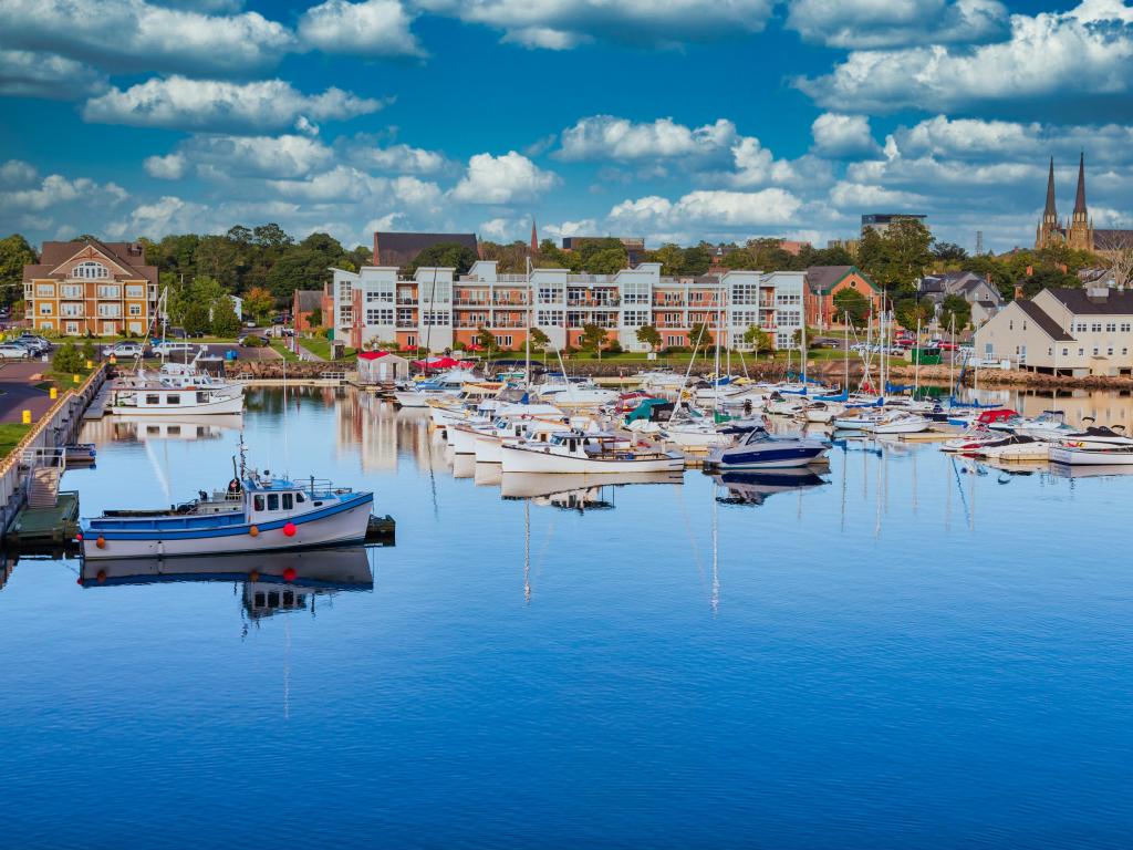 Charlottetown, Prince Edward Island in Canada with small fishing boats in a calm blue harbor and the city buildings in the distance on a sunny day.