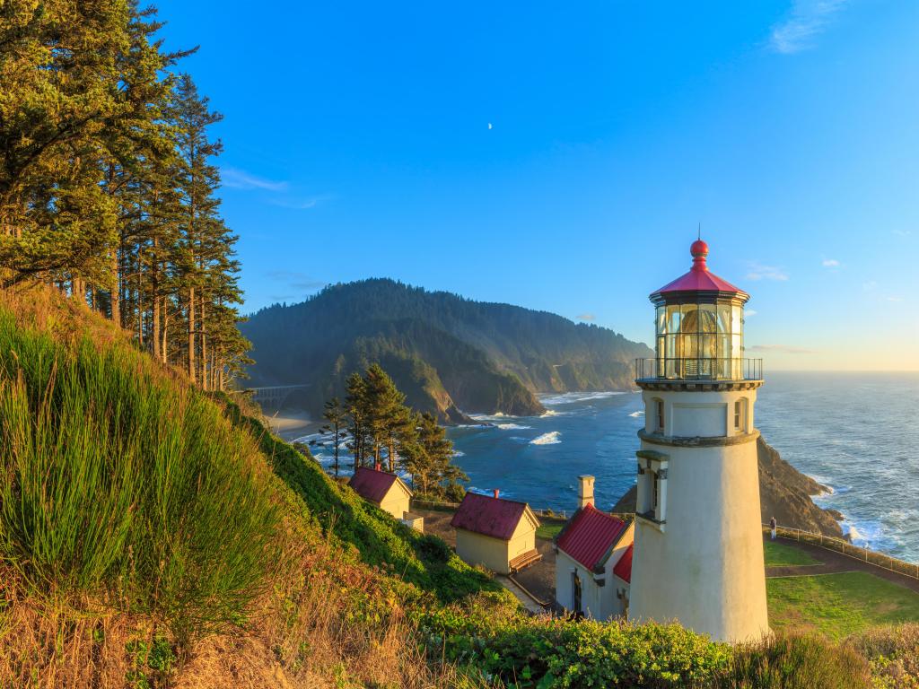 Heceta Head Lighthouse, Oregon with the sun setting in the distance and the lighthouse overlooking the sea below. 
