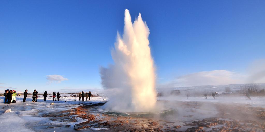 A geyser firing from the ground with people watching in Iceland 