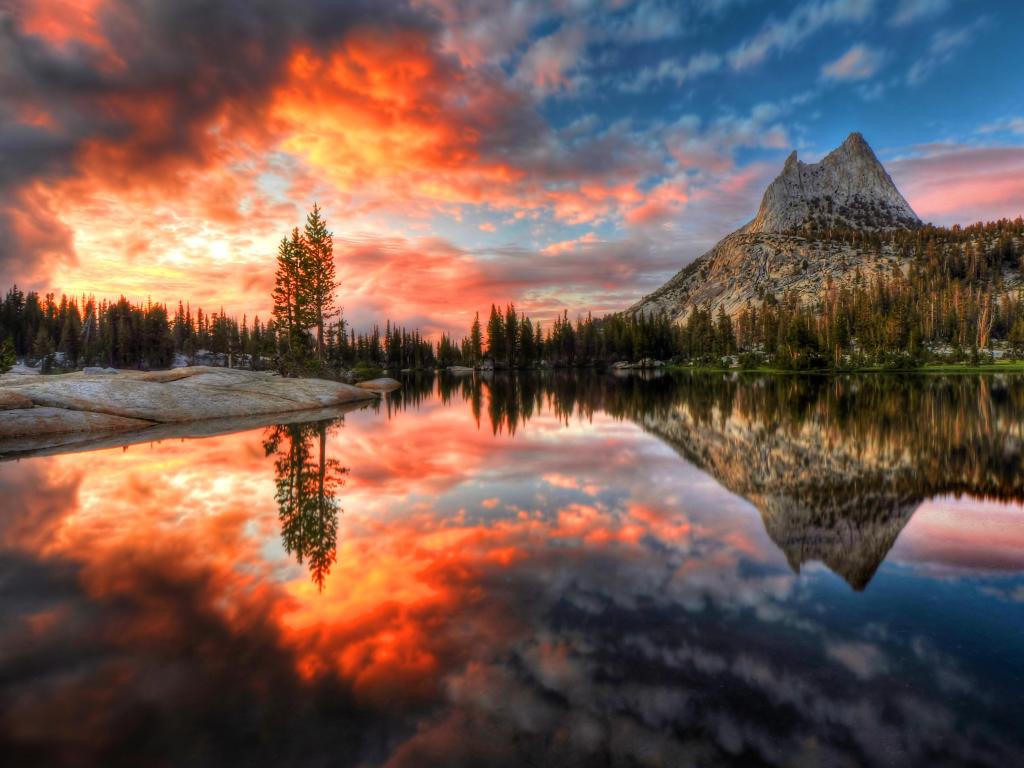 Last Light at Cathedral Lake Yosemite National Park, California, during a fiery sunset. There is a lake in the foreground that reflects the scene.