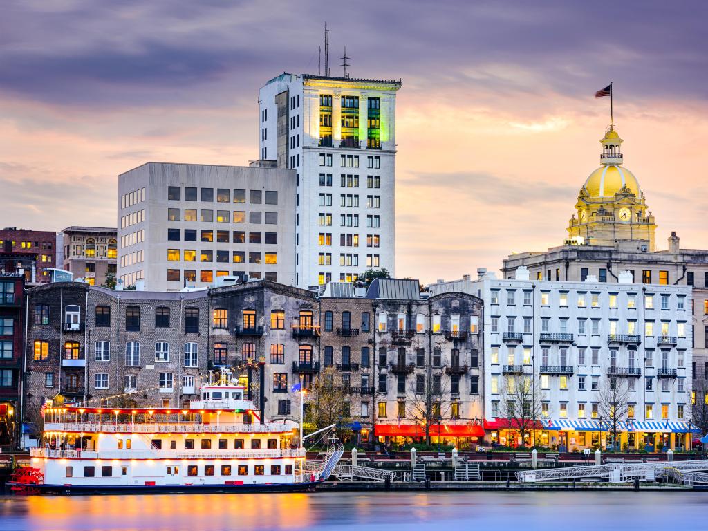 Savannah, Georgia, USA downtown skyline at sunset. You can see one of the famous steamboats docked with historic buildings in the background.