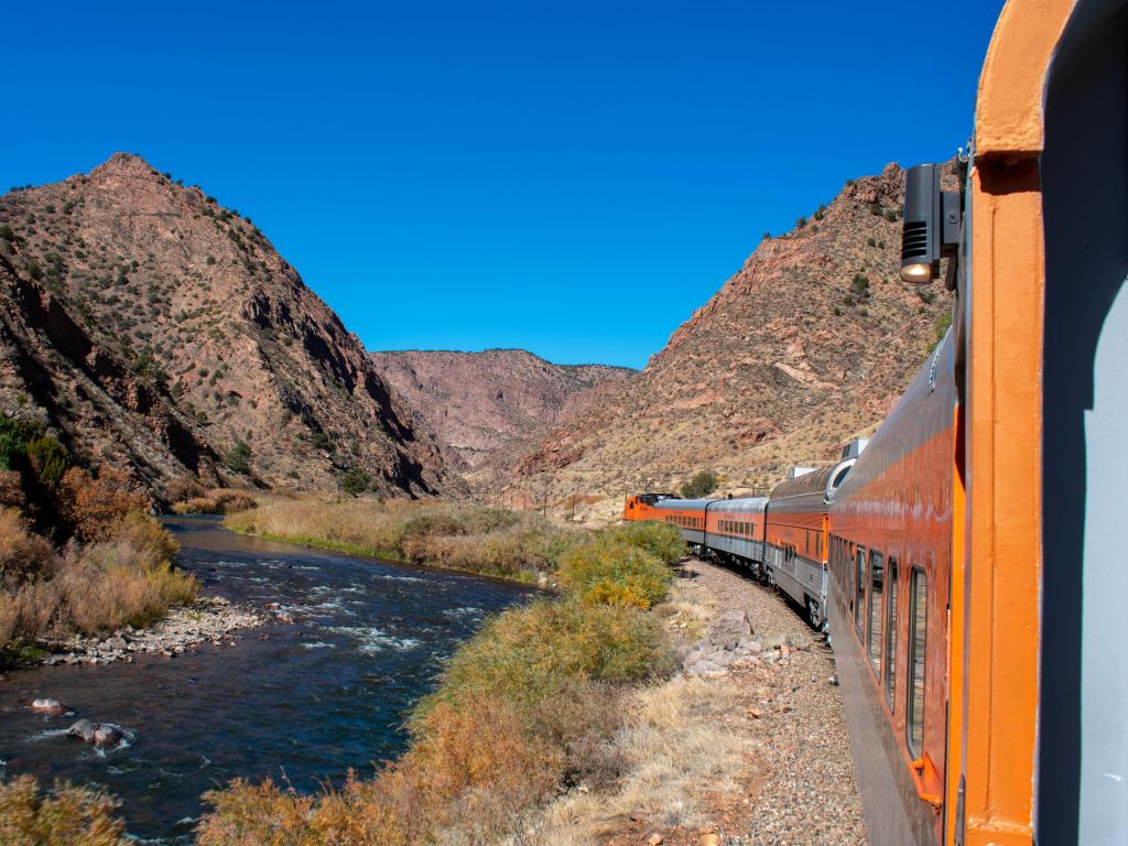 Scenic railroad by the Arkansas River, orange train cars through the gorge