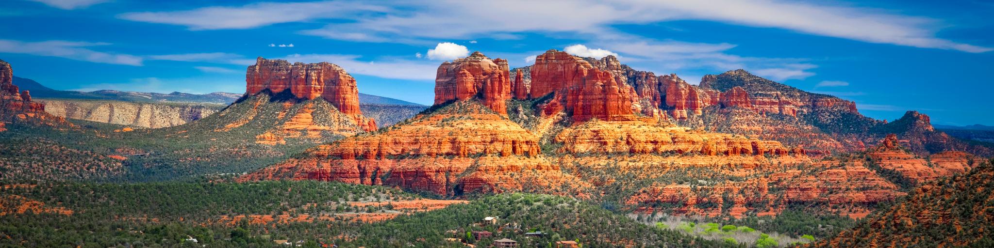 A Panoramic View of Red Rock Mountain with a beautiful sight of green trees' and a cloudy blue sky in Sedona, Arizona.