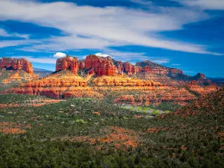 A Panoramic View of Red Rock Mountain with a beautiful sight of green trees' and a cloudy blue sky in Sedona, Arizona.