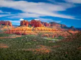 A Panoramic View of Red Rock Mountain with a beautiful sight of green trees' and a cloudy blue sky in Sedona, Arizona.