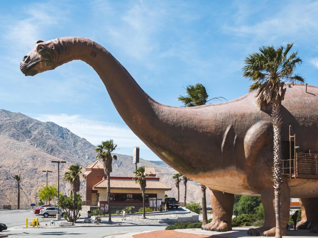 Cabazon Dinosaur statue stands tall next to a Burger King restaurant in California, with desert mountains behind