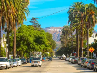 Hollywood sign district in Los Angeles, USA. Beautiful Hollywood highway road with cars, palms and a sign on the hills. Clear blue sky.