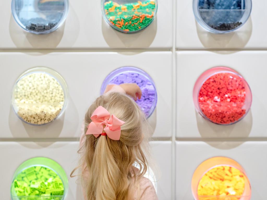 View of a young girl choosing Lego pieces in the Lego store in Gurnee, IL. Shot from behind, the girl wears her hair tied back in a pink bow