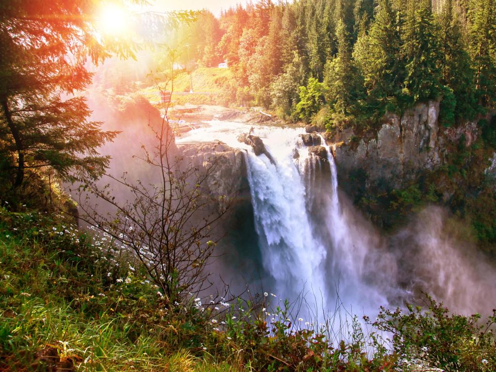 Snoqualmie Falls, Washington State, USA with the morning sun peeking through the trees and a stunning waterfall surrounded by dense trees. 