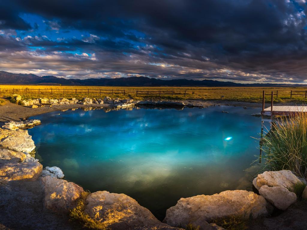 Panoramic view of Meadow Hot Spring at sunset, with light blue spring waters against darkening evening sky, and surrounding grasslands