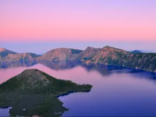 Oregon, USA with a beautiful view of Crater Lake at sunset with hills in the distance and a pink sky.