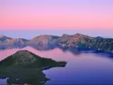 Oregon, USA with a beautiful view of Crater Lake at sunset with hills in the distance and a pink sky.