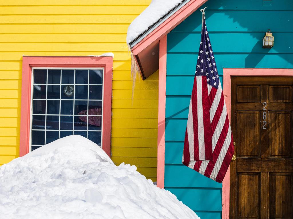 A brightly colored wooden house, blanketed in snow, stands in the small town of Minturn, Colorado, with a US flag outside the door