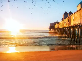 Portland, Maine, USA taken at dawn with waves crashing against an old wooden pier and a flock of birds in the sky. 