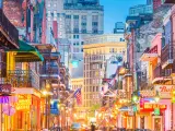 Bright lights and shop signs shine outside low rise houses with metal balconies along Bourbon Street, New Orleans at dawn