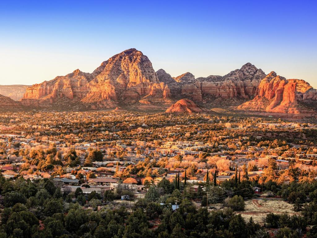 Sedona, Arizona, USA with a birds eye view to the city of Sedona, Arizona and the Red Rocks at sunset against a blue sky.
