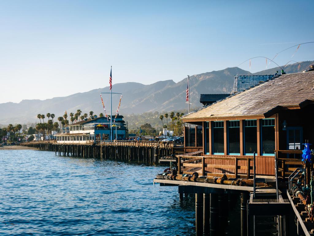 Wooden wharf juts out into the ocean, mountains and palm trees behind
