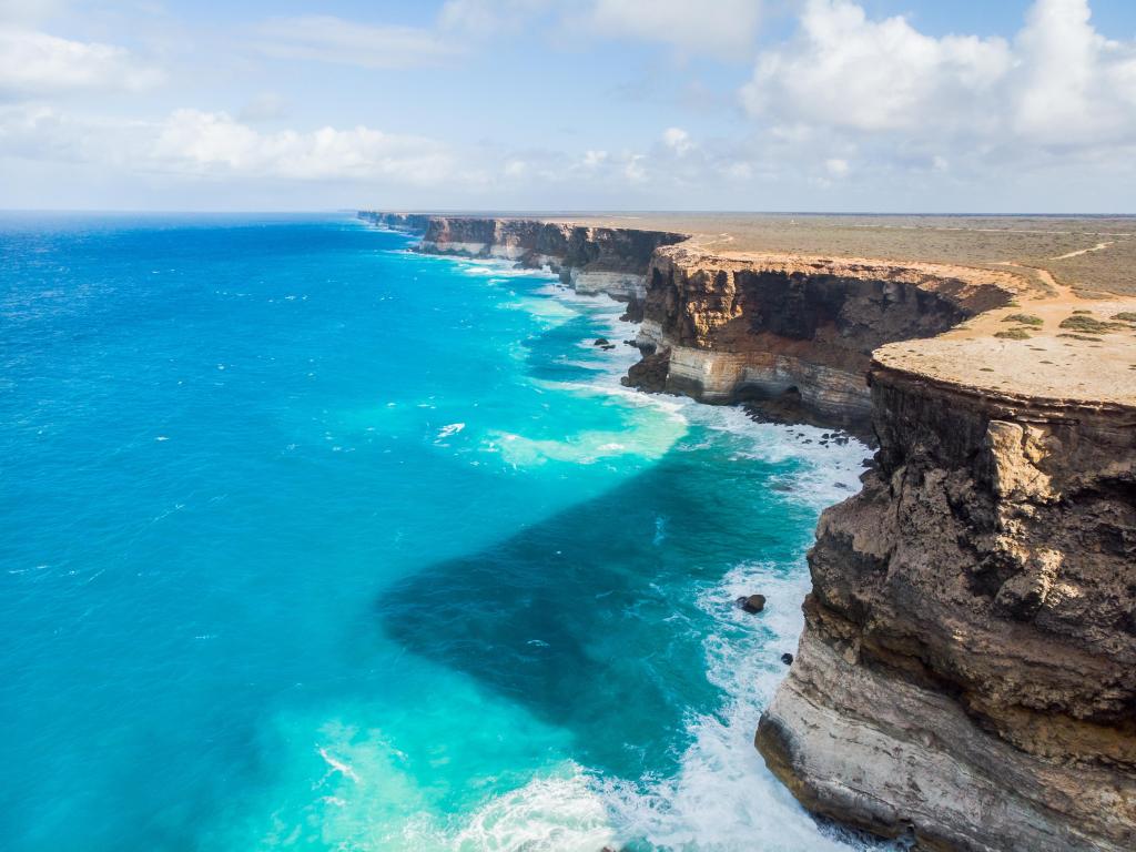 Tall sea cliffs viewed from above with bright blue ocean and waves breaking benneath