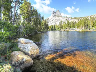 Up close view of clear Upper Cathedral Lake sitting below Cathedral Peak, with surrounding forests and boulder dotted shoreline