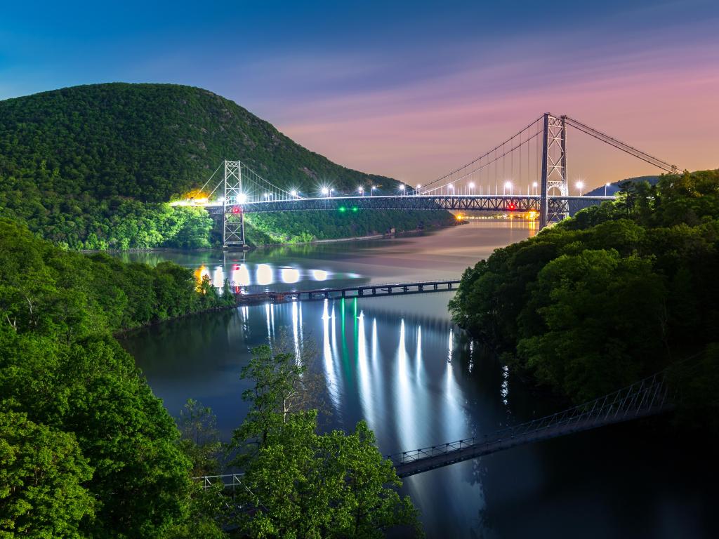 Night time view of illuminated bridge across steep-sided river valley with hillsides covered in green trees