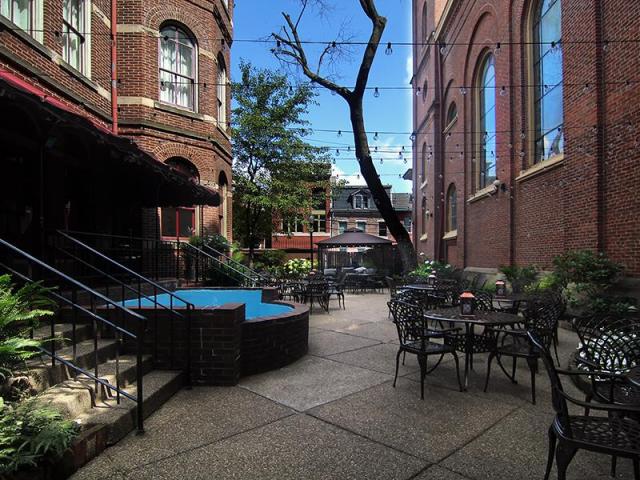 Outdoor terrace, with chairs and tables and hanging lights across paved courtyard.