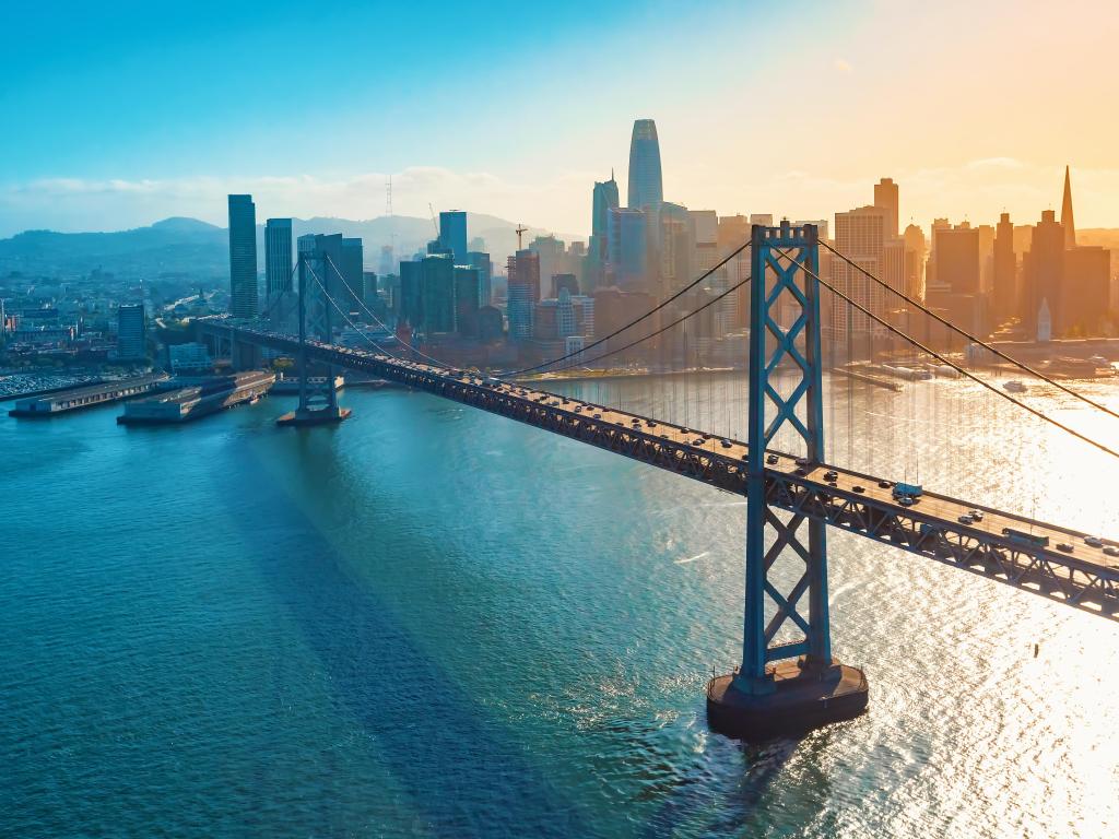 San Francisco, CA, USA with an aerial view of the Bay Bridge taken at sunset with the city skyline in the background. 