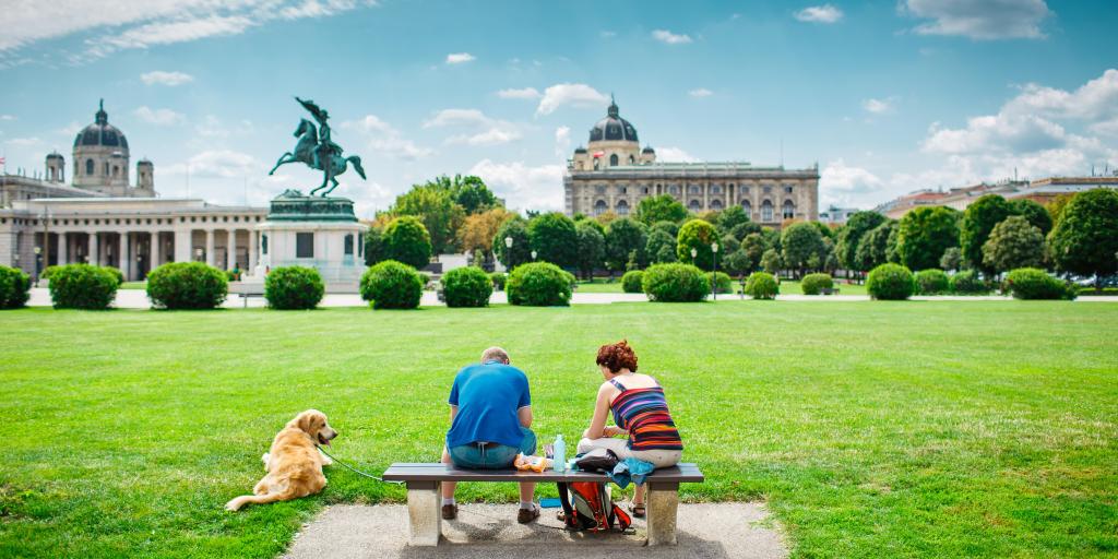 Two friends sitting on the bench with beautiful view to Vienna panorama with a dog 