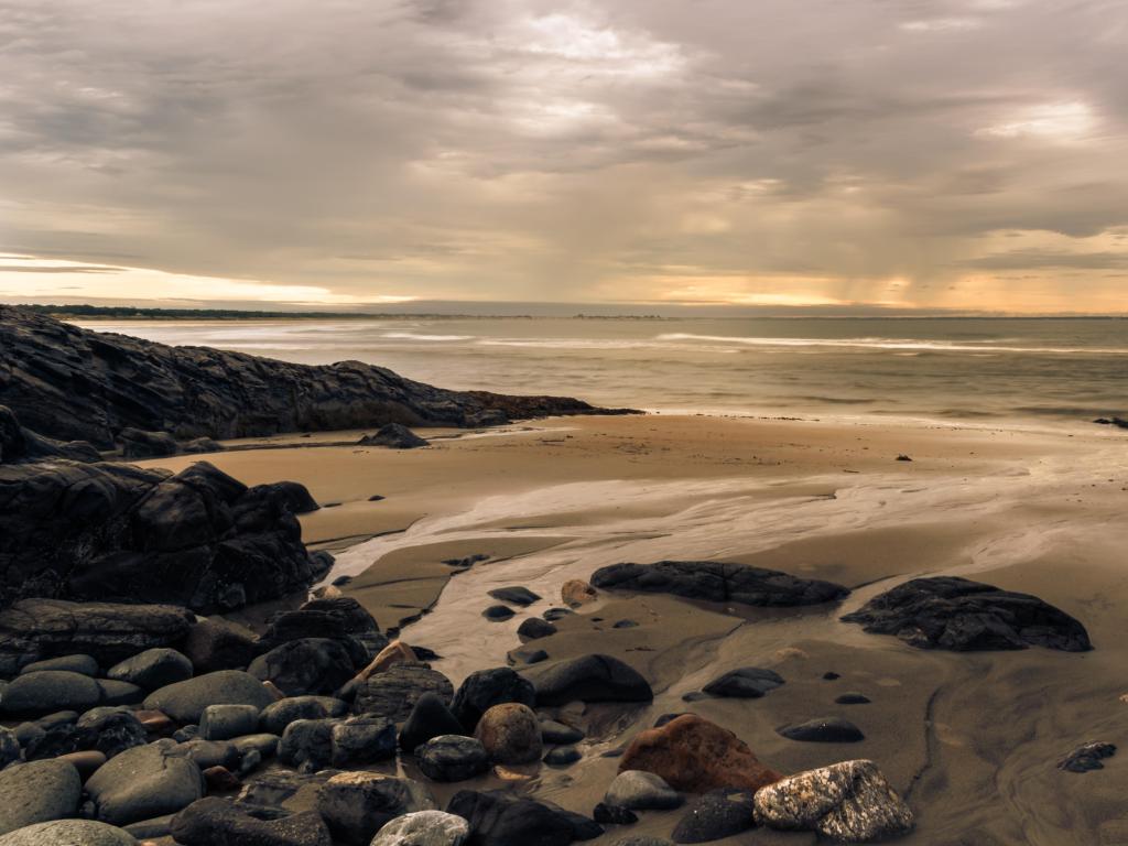 Ogunquit Beach, Maine, USA taken at sunrise with rocks in the beach in the foreground and the sea and a cloudy sky in the distance. 