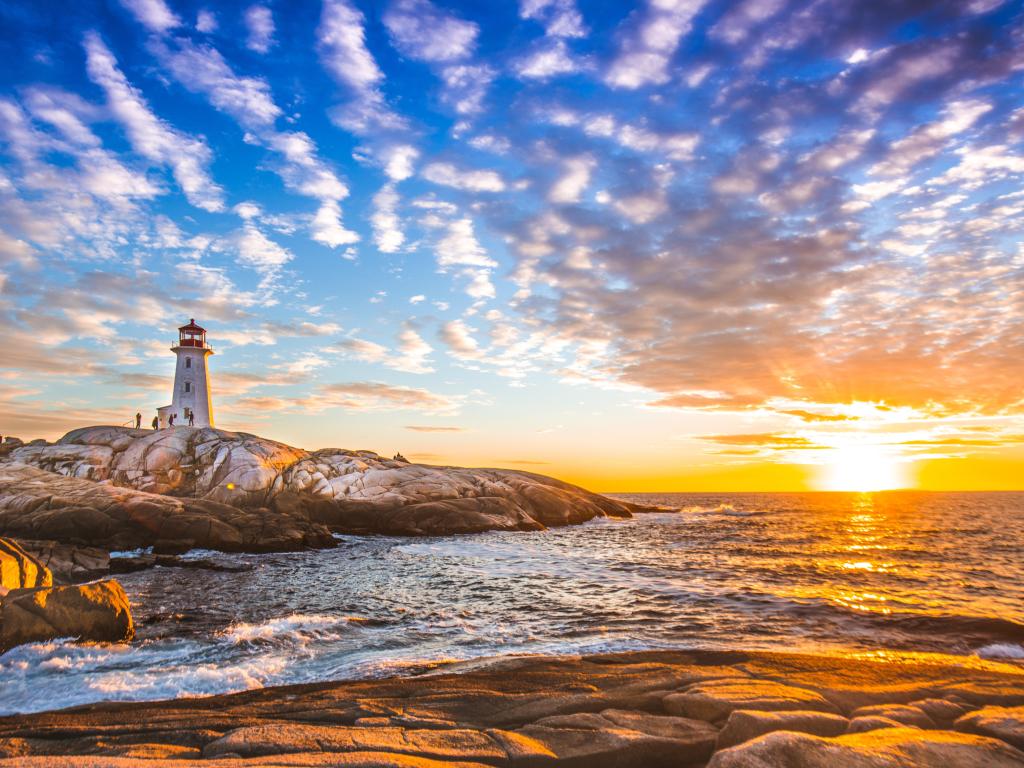 White lighthouse on smooth rocks beside calm sea with vivid gold sunset light