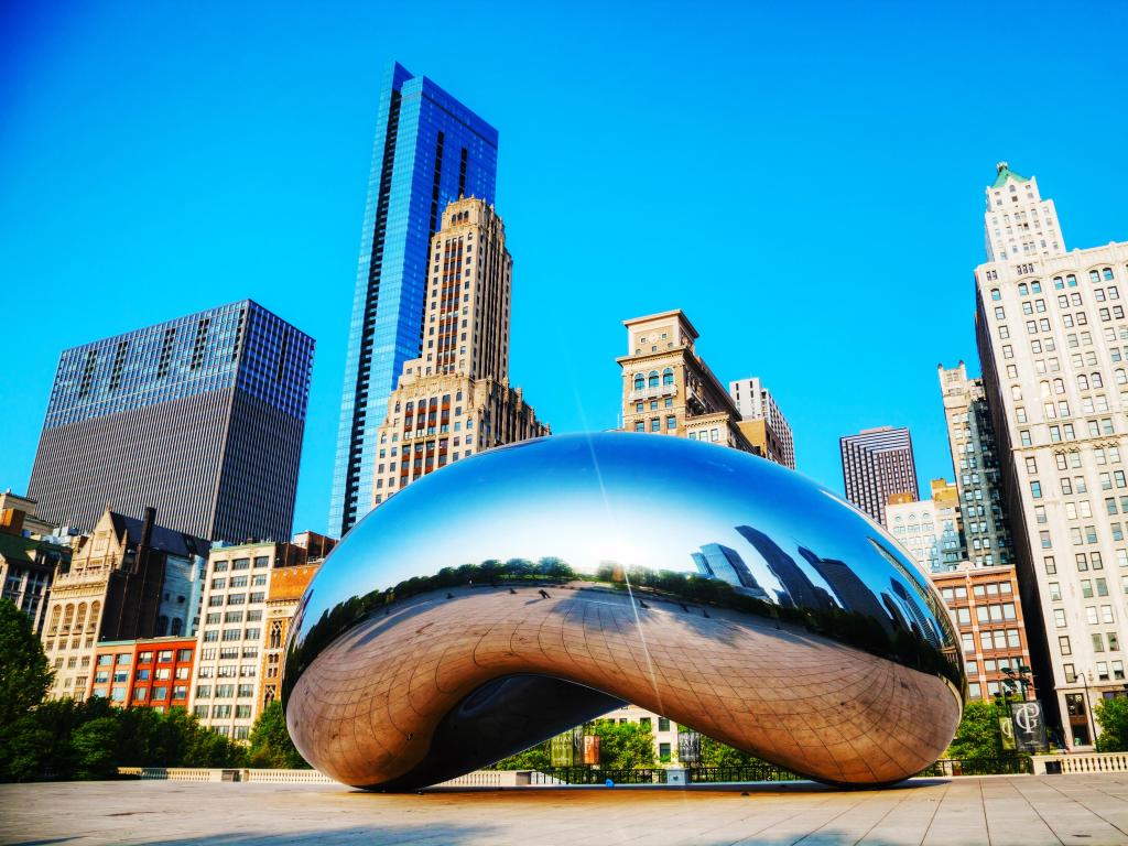 Silver arched sculpture stands in bright sunlight in front of high rise buildings