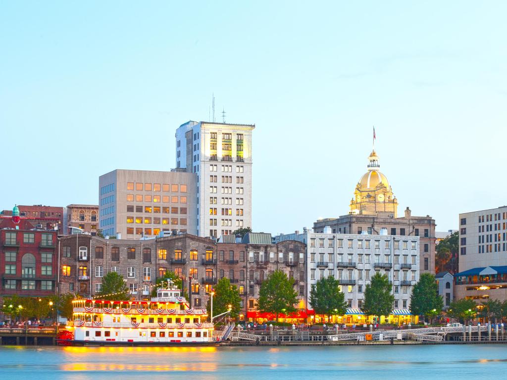 The view of the historic downtown across the water during sunset, with a lit-up riverboat in view